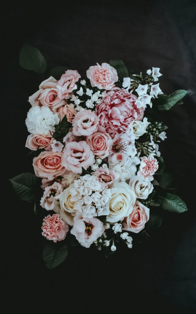 Arrangement floral de deuil composé de pivoines et de roses sur fond noir.